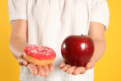 Concept of choice. Woman holding apple and doughnut on yellow background, closeup