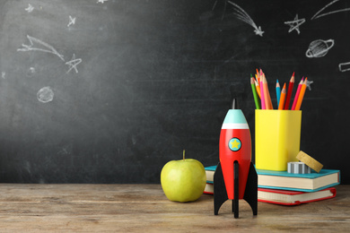 Bright toy rocket and school supplies on wooden desk. Space for text