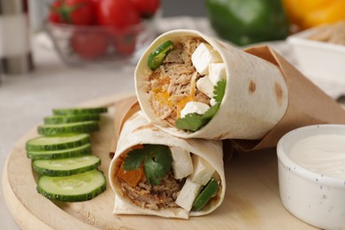 Photo of Delicious tortilla wraps with tuna, cucumber slices and sauce on wooden board, closeup