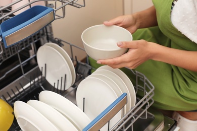 Photo of Young woman loading dishwasher in kitchen, closeup. Cleaning chores