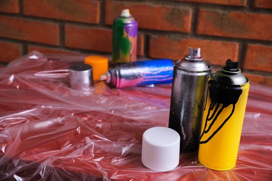 Used cans of spray paints on table near brick wall, space for text. Graffiti supplies