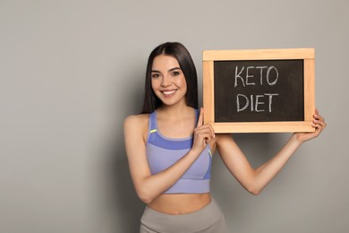 Happy woman holding chalkboard with words Keto Diet on light grey background