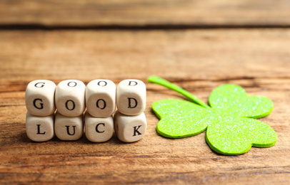 Cubes with phrase GOOD LUCK and clover leaf on wooden table