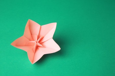 Photo of Origami art. Handmade pink paper flower on green background, above view with space for text