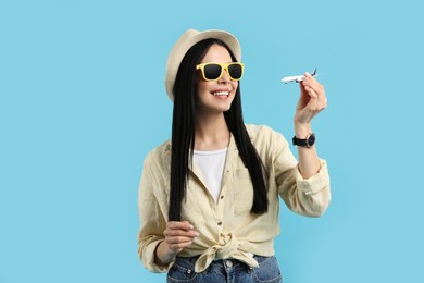 Photo of Happy female tourist with toy plane on light blue background