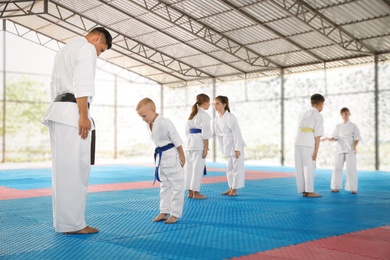 Children and coach in kimono performing ritual bow before karate practice on tatami outdoors