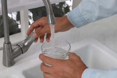 Man filling glass with water from tap at home, closeup