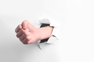 Man breaking through white paper with fist, closeup. Space for text