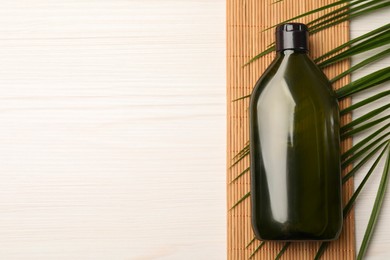 Photo of Shampoo bottle, bamboo mat and green leaf on white wooden table, flat lay. Space for text