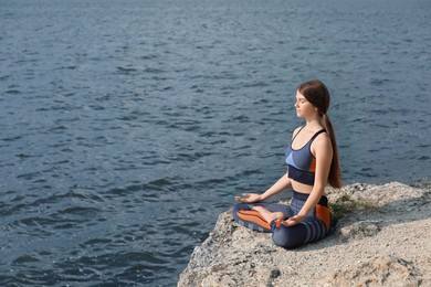 Teenage girl meditating on cliff near river. Space for text
