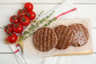 Tasty grilled hamburger patties, cherry tomatoes and thyme on white wooden table, flat lay