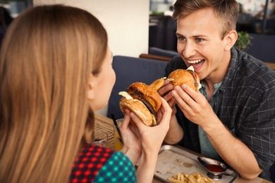 Photo of Young couple eating burgers in street cafe
