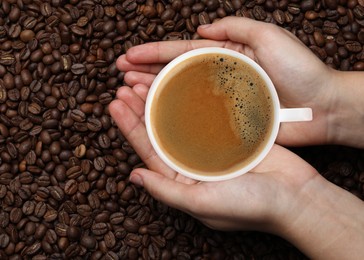 Image of Woman with cup of tasty espresso and roasted coffee beans, top view