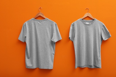 Hangers with blank t-shirts on color background. Mockup for design