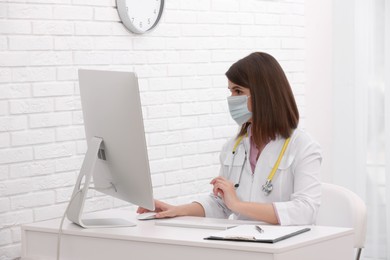 Pediatrician in protective mask consulting patient online at table indoors