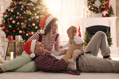 Happy family with cute baby on floor in room decorated for Christmas