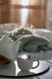 Tray with cup of hot tea and teapot on bed indoors