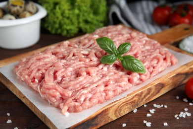 Raw chicken minced meat with basil and salt on wooden table, closeup