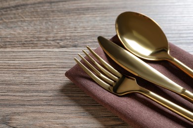Set of golden cutlery with napkin on wooden table, closeup. Space for text