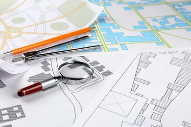 Office stationery and magnifying glass on cadastral maps of territory with buildings