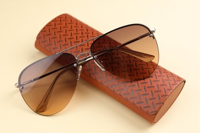 Stylish sunglasses and brown leather case with pattern on beige background