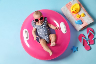 Cute little baby in sunglasses with inflatable ring and beach accessories on light blue background, top view