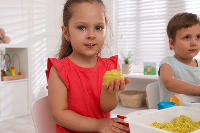 Cute little children playing with bright kinetic sand at table in room