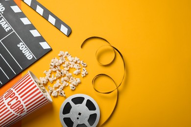 Clapperboard, popcorn and film reel on orange background, flat lay. Space for text