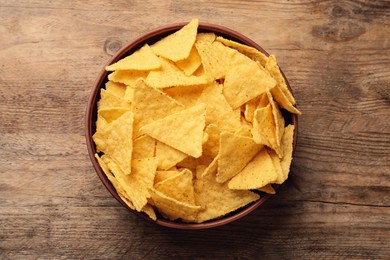 Photo of Bowl of tasty tortilla chips (nachos) on wooden table, top view