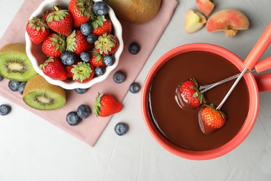 Dipping strawberries into fondue pot with chocolate on grey table, top view
