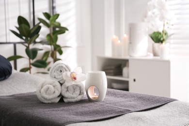 Photo of Towels, aroma lamp and orchid flower on couch in spa salon