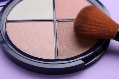 Photo of Colorful contouring palette with brush on violet background, closeup. Professional cosmetic product