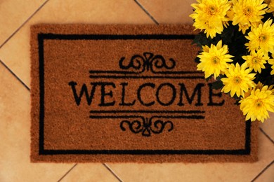 Door mat with word Welcome and beautiful flowers on floor, flat lay