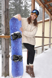 Young woman with snowboard wearing winter sport clothes and goggles outdoors