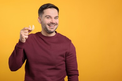 Photo of Happy man holding tasty fortune cookie with prediction on orange background. Space for text