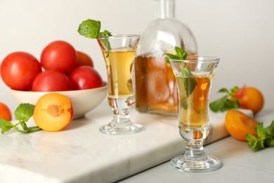 Delicious plum liquor with mint and ripe fruits on light table. Homemade strong alcoholic beverage