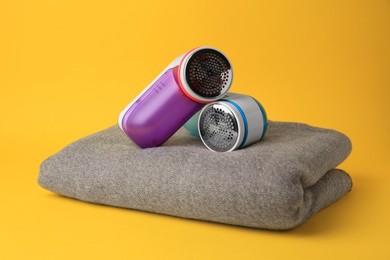 Photo of Modern fabric shavers and woolen clothes on yellow background
