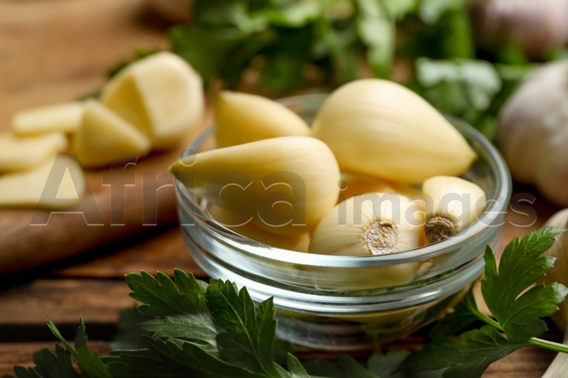 Fresh peeled garlic cloves in bowl and parsley on wooden table, closeup. Organic product