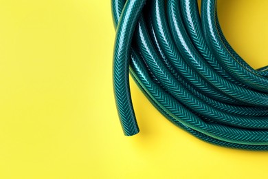 Green rubber watering hose on yellow background, top view. Space for text