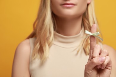 Photo of Woman showing index finger with tied bow as reminder on orange background, closeup