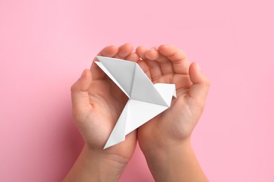 Photo of Origami art. Child holding paper bird on pink background, top view