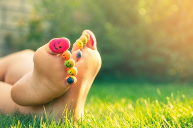 Teenage girl with smiling faces drawn on toes outdoors, closeup. Space for text