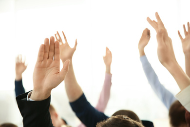 People raising hands to ask questions at business training on light background, closeup
