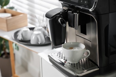 Modern coffee machine with cup of cappuccino in office. Space for text