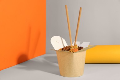 Box of wok noodles with seafood and chopsticks on color background. Space for text