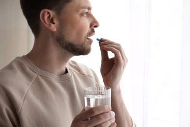 Man with glass of water taking pill at home