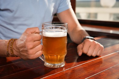 Man with glass of tasty beer at wooden table in pub, closeup