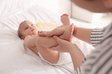 Mother massaging her cute baby with oil on bed at home, closeup