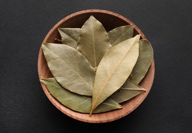 Bay leaves in wooden bowl on black background, top view