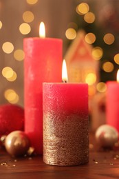 Beautiful burning candles with Christmas decor on wooden table against blurred festive lights